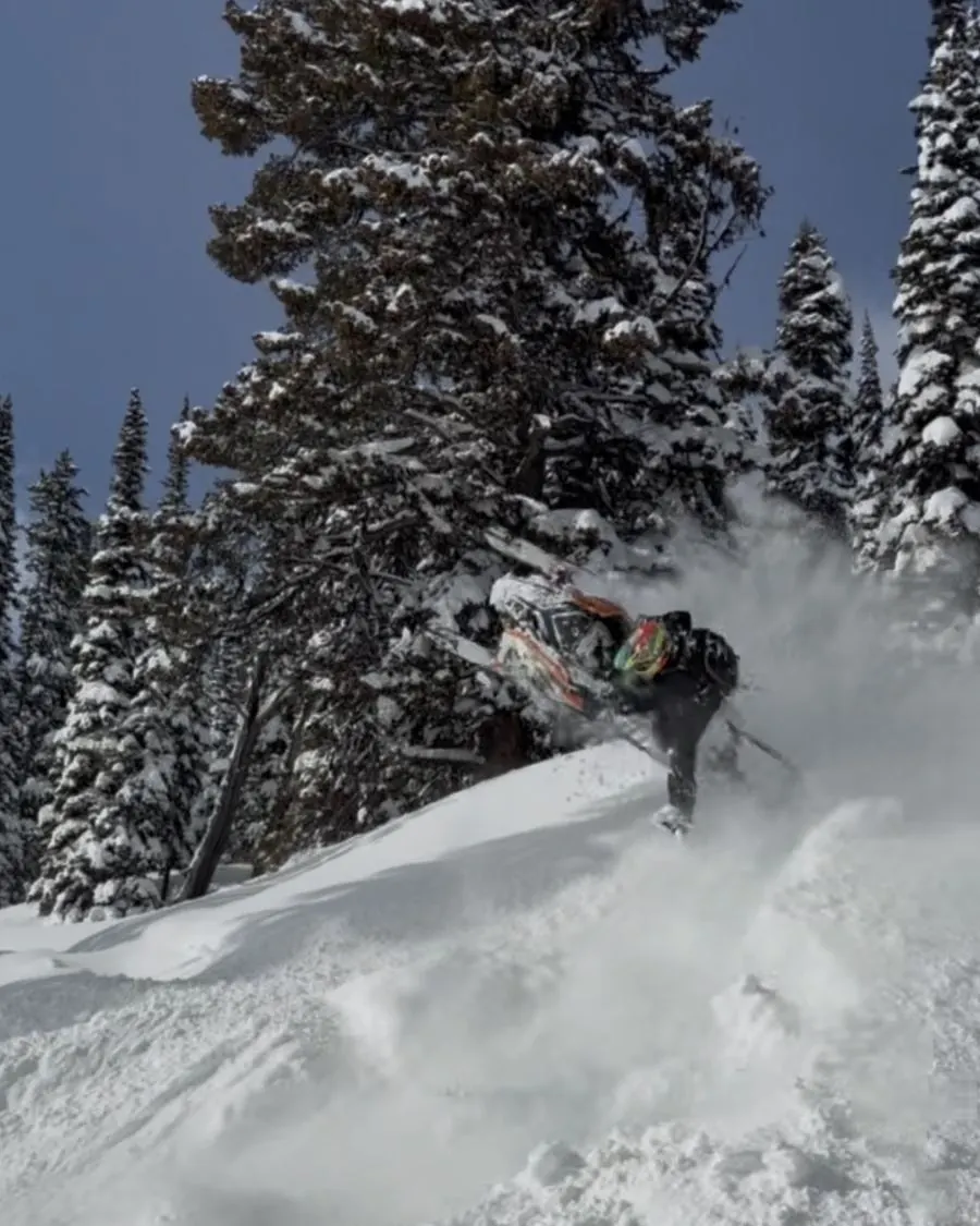 Snowmobile rider carving along a snowy ridge